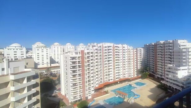 Ein Hochhaus mit mehreren Balkonen, einem Schwimmbad und blauem Himmel.