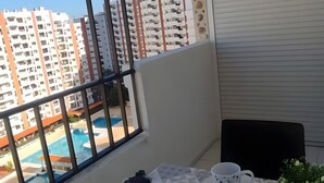 Ein Balkon mit Tisch für zwei Personen, Blick auf ein Schwimmbecken und hohe Gebäude im Hintergrund.