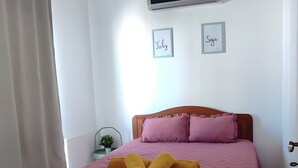 Ein Schlafzimmer mit einem Bett, einem Nachttisch, einer Wand-Klimaanlage und zwei gerahmten Bildern.