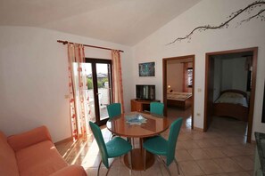A room with a round glass table, four chairs, a sofa, a bed, a TV, and a painting on the wall. - Holiday apartment with balcony and barbecue (Funtana)