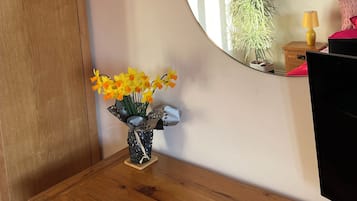 A wooden dresser with a vase of yellow flowers, a round mirror, and a small plant on a bedside table.