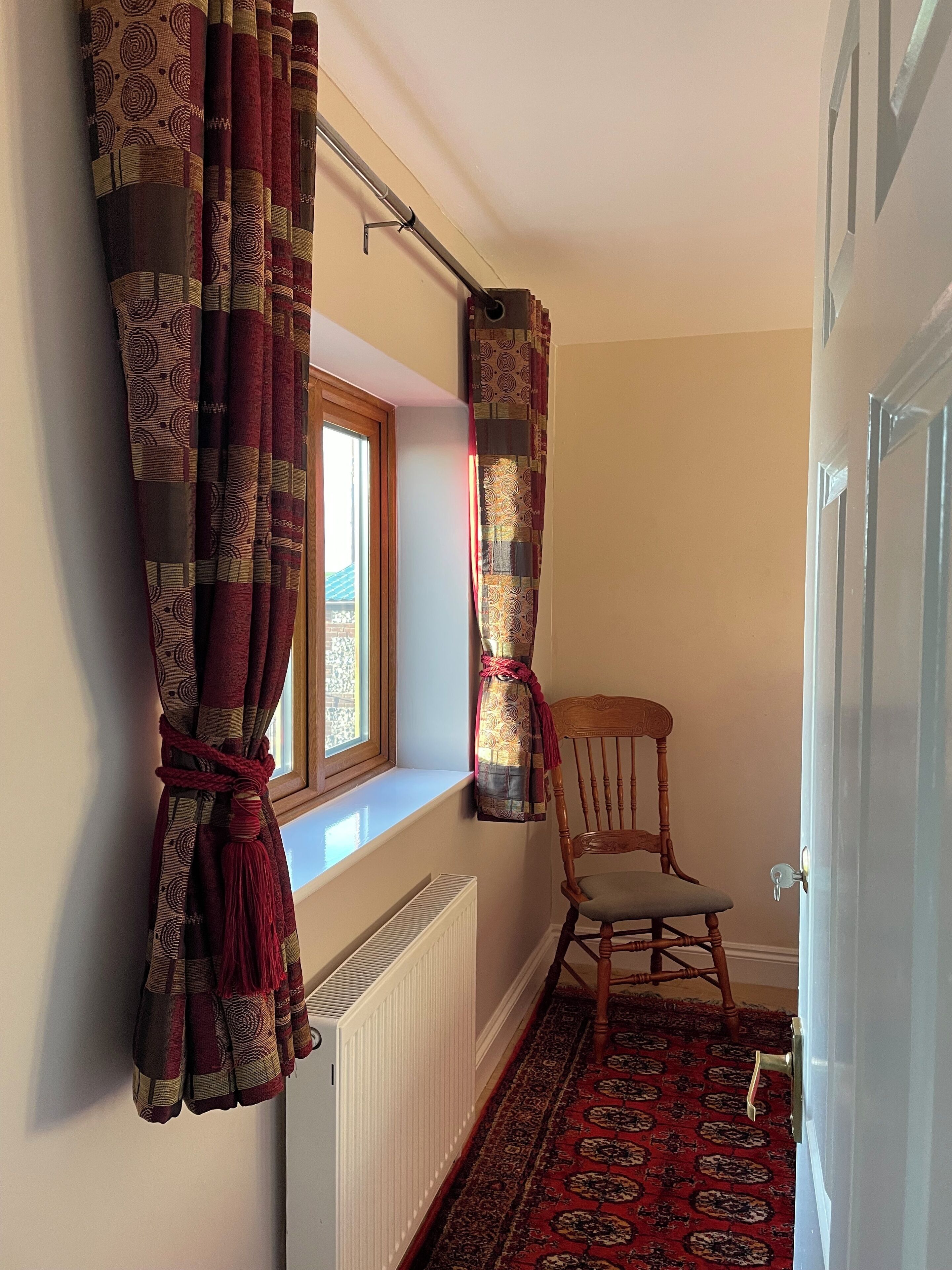 A room with a radiator, a window with curtains, a wooden chair, and a patterned carpet.