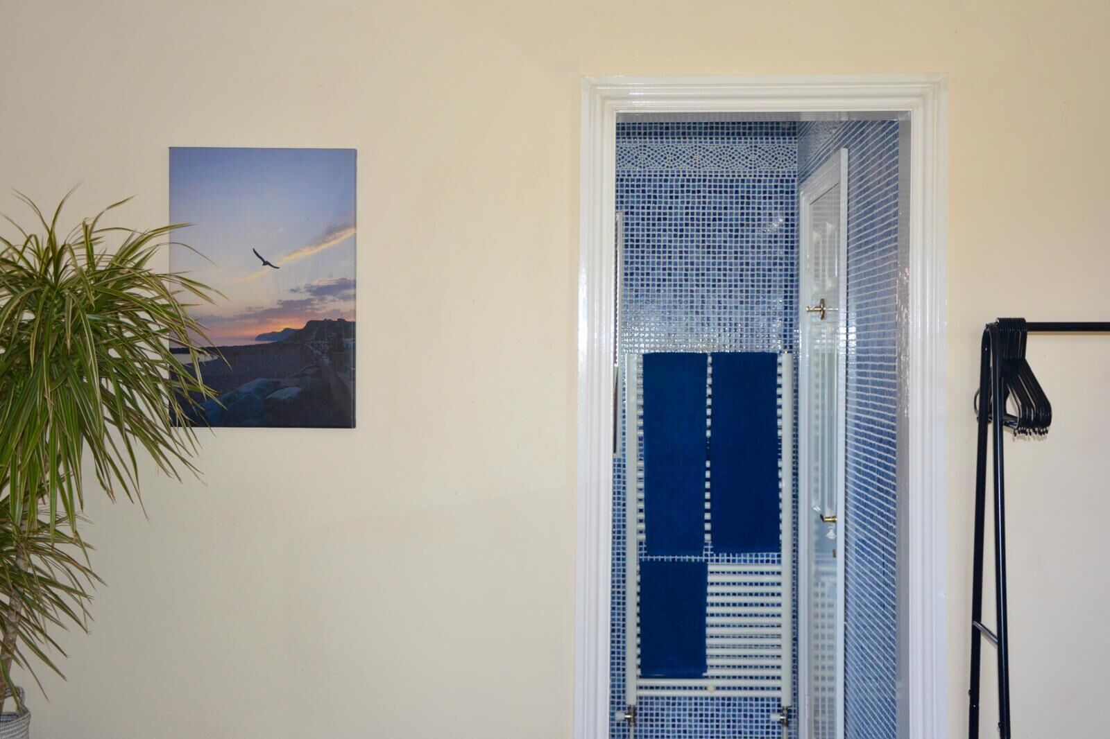 Una habitación con puerta a un balcón, una planta en maceta y un cuadro en la pared.