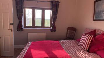 A bedroom with a bed, a radiator, a window with curtains, a chair, and a painting on the wall.