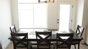 A dining room with a dark wooden table and chairs, a chandelier, and large windows. - Modern Mapleton Retreat (Spanish Fork)