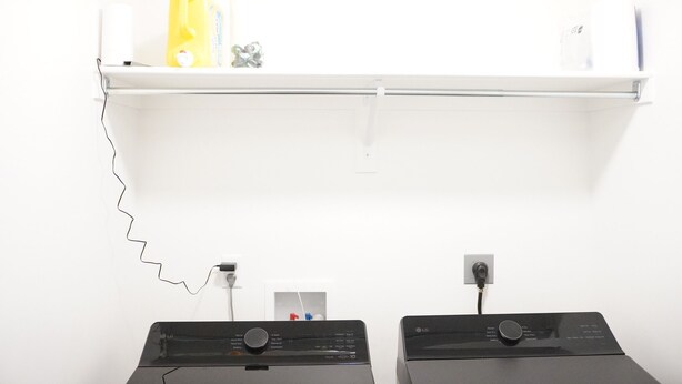 Ett rum med en vit vägg, en hylla med en gul flaska och tv å svarta elektroniska apparater.