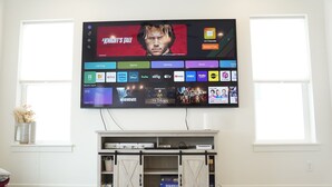 En platt-TV som är monterad på en vägg ovanför ett träinrett TV-möblemang med en skjutbar dörr i stil med en ladugårdsdörr.