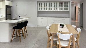 A modern kitchen with white cabinets, a central island with bar stools, and a dining area with a wooden table and white chairs. - Modern Luxury with Nature (Spring Farm)
