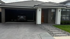 A residential garage with a vehicle inside, a driveway leading to a house with a tiled roof, and a small garden area with stepping stones. - Modern Luxury with Nature (Spring Farm)