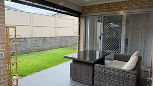 A patio area with a table and chairs, a wooden ladder, and a view of a backyard with a lawn and a brick wall. - Modern Luxury with Nature (Spring Farm)