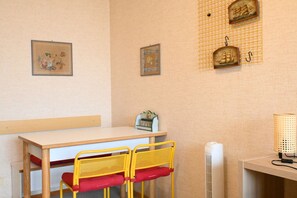 A room with a wooden table, two yellow chairs with red cushions, a white radiator, and wall-mounted artwork.