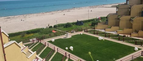 A beach view from a balcony with a grassy area and a pool.