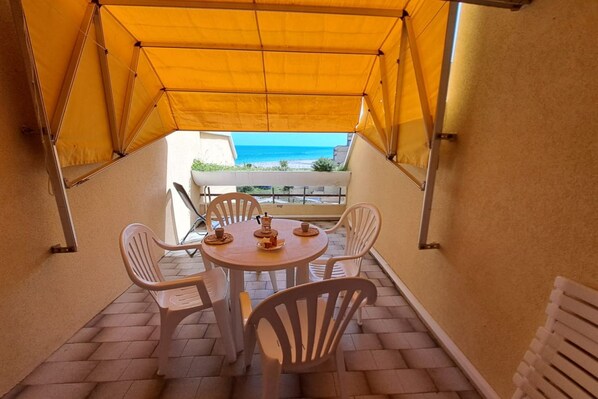 A covered outdoor seating area with a table and chairs, overlooking a beach.