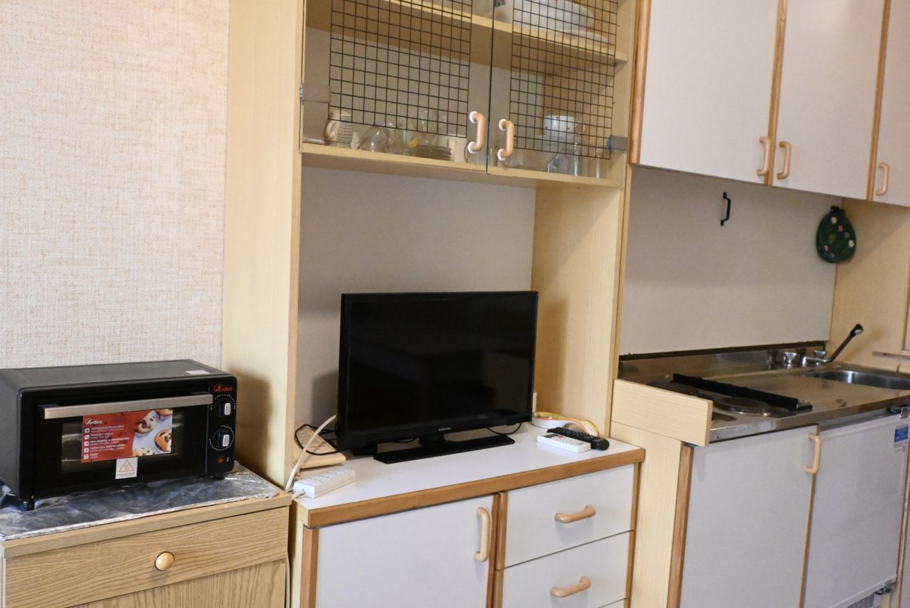 Een kitchenette met een magnetron, een televisie, een spoelbak en een kastje met een ruitpatroon.