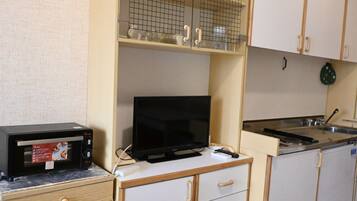 Een kitchenette met een magnetron, een televisie, een spoelbak en een kastje met een ruitpatroon.