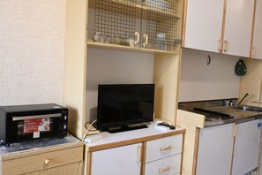 A kitchenette with a microwave, a television, a sink, and a cabinet with a grid-like window.