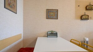 Una habitación pequeña con una mesa blanca, un banco rojo, un cuadro enmarcado y una repisa con adornos.