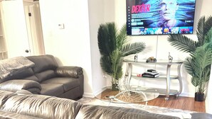 Un saló amb un sofà de cuir gris, una taula de centre de vidre i un televisió de pantalla plana penjada a la paret que mostra 'DEXTER'.