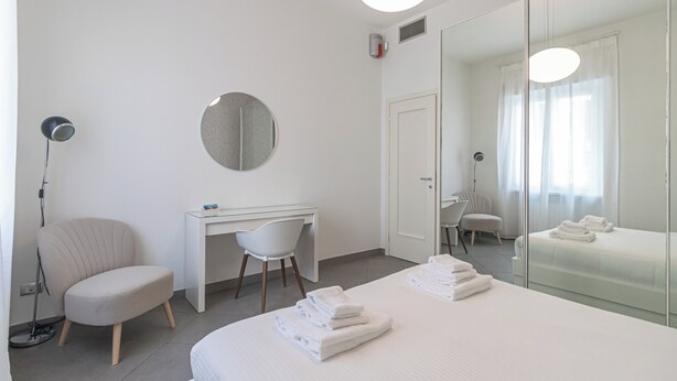 Una habitación de hotel moderna con una cama, un escritorio, una silla, un espejo redondo y una lámpara de pie.
