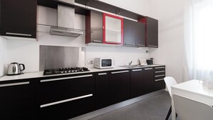 Cocina moderna con gabinetes negros, encimera blanca, campana extractora de acero inoxidable, microondas y cafetera.