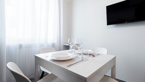 Un comedor moderno con una mesa blanca dispuesta para dos personas, incluyendo platos, vasos y cubiertos.