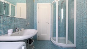 Un baño con un lavamanos blanco, un espejo, una ducha con puerta de vidrio y paredes con azulejos azules.