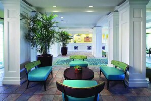 A lobby with a reception desk, seating area with chairs and a table, and potted plants.