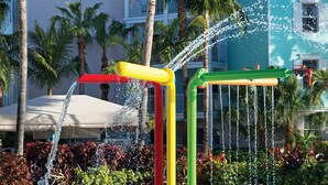 Una fuente con múltiples chorros de agua, rodeada de palmeras y un edificio con balcones.