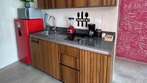 Cocina compacta con armarios de madera, un refrigerador rojo, un lavamanos y una cafetera.