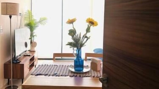 Una habitación con una mesa de madera, un jarrón azul con flores, una lámpara y un ventilador de techo.