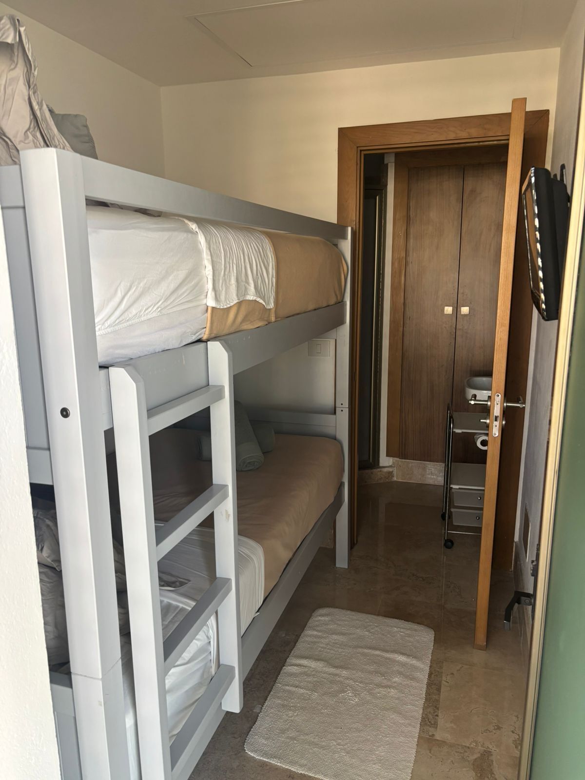 Une chambre avec un lit superposé, une porte en bois et un petit meuble de rangement.