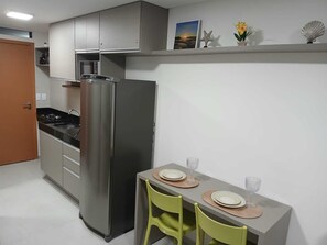 A compact kitchen with a refrigerator, a sink, and a dining table with chairs. - Flat no centro de Porto de Galinhas  (Ipojuca)