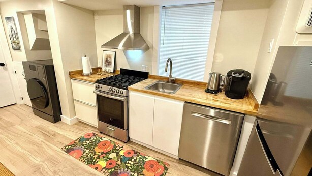 Una cocina compacta con estufa, lavaplatos y lavadora, además de un ventanal con persianas.