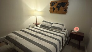 Un dormitorio con cama, mesita de noche, lámpara y un mapa del mundo en la pared.