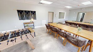 A spacious room with a long wooden table and wicker chairs, a foosball table, and a small shelf with plants. - 4 Bedroom Condo In Pigeon Forge- Unit 711, 4 Bedroom Condo In Pigeon Forge- Unit 711 (Pigeon Forge)
