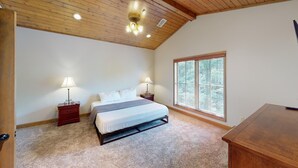 A bedroom with a wooden ceiling, a large bed, two bedside tables with lamps, a window with blinds, and a wooden dresser. - 1 Bedroom Condo by Dollywood- Unit 321, 1 Bedroom Condo by Dollywood- Unit 321 (Pigeon Forge)