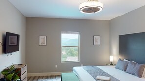 Ein Schlafzimmer mit einem großen Bett, einem Fenster mit Bergblick, einem Nachttisch mit Lampe und einem an der Wand befestigten Fernseher.