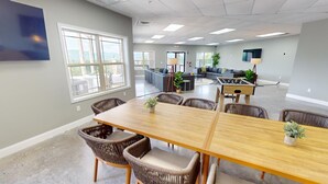 Una amplia sala de reuniones con una larga mesa de madera, sillas de mimbre y grandes ventanales que ofrecen vistas al exterior.