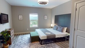 A modern bedroom with a bed, bedside tables, a window, and a view of the outdoors. - NEW 2 Bedroom Condo in Pigeon Forge- Unit 4, NEW 2 Bedroom Modern Mountain Escape - Club House Unit (Pigeon Forge)