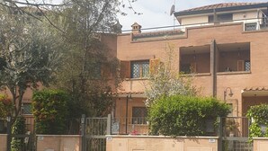 A courtyard with a brick building, a gate, and a tree with white flowers. - Villa "Domus Roma" - Room Piazza Navona (Roma)