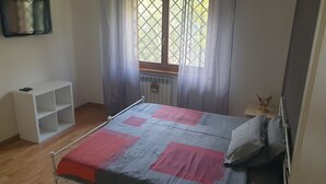 A bedroom with a bed, a white shelf unit, a radiator, and a window with curtains. - Villa "Domus Roma" - Room Piazza Navona (Roma)