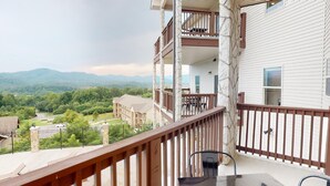 Un balcon donnant sur un paysage montagneux, un pilier en pierre et une table avec des chaises.