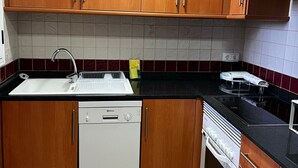 A kitchen with wooden cabinets, a dishwasher, an oven, and a black countertop. - Playasol in Denia With 3 Bedrooms and 2 Bathrooms (Denia)