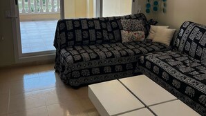 A living room with a patterned sofa, a white coffee table, and a view through a sliding glass door to a balcony. - Playasol in Denia With 3 Bedrooms and 2 Bathrooms (Denia)