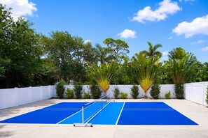 An outdoor tennis court with a white fence, blue surface, and trees in the background. - Walk to the Beach (Sarasota)