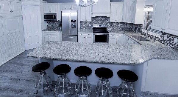 A modern kitchen with white cabinetry, a granite countertop, a stainless steel refrigerator, and a built-in oven. - Walk to the Beach (Sarasota)