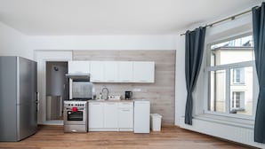 A modern kitchen with white cabinets, stainless steel appliances, and a window with curtains. - Kilińskiego Standard Apartment (Łódź)