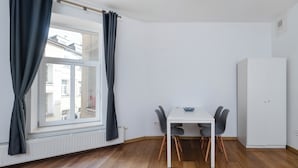 A room with a dining table, four chairs, a white cabinet, and a window with curtains. - Kilińskiego Standard Apartment (Łódź)