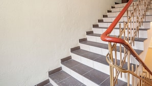A staircase with a red handrail and wooden balusters, leading to a door with a handle. - Kilińskiego Standard Apartment (Łódź)