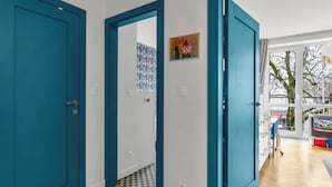 Ein Flur mit türkisfarbenen Türen, einem Schachbrettfußboden und einem Fenster mit Blick auf Bäume und ein Gebäude.